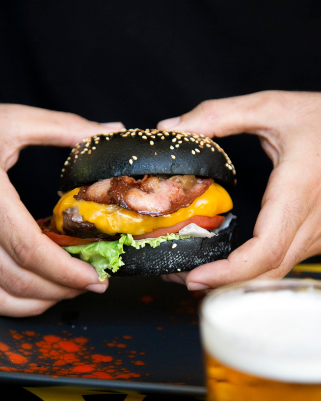 Hamburguesa con pan de carbón activo y probióticos, cheddar, beicon, cebolla caramelizada y tomate confitado.