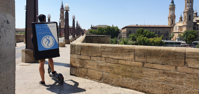 Carlos Sánchez, el fisio sobre ruedas, con su patinete y camilla, en el puente de Piedra de Zaragoza, este viernes.