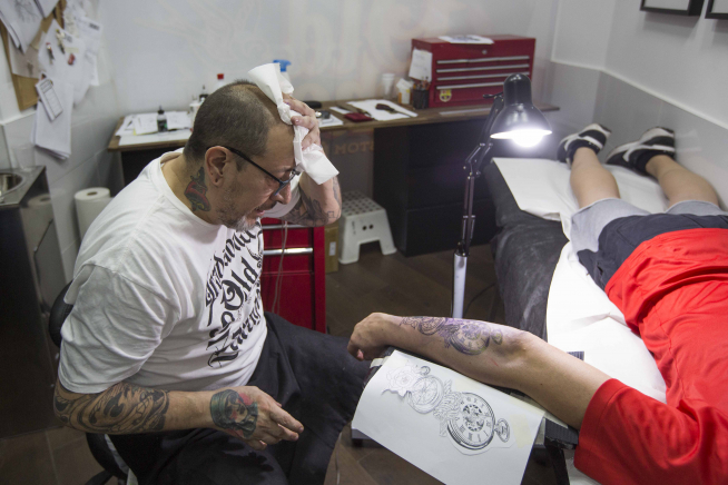 Horacio Febre se seca la frente de sudor mientras realiza un tatuaje.