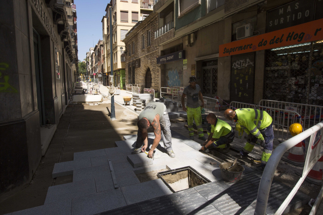 Varios trabajadores colocan baldosas en la calle de San Miguel.