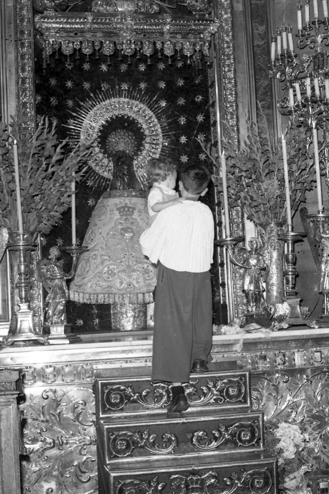 Un infantico lleva a un niño para pasarlo por el manto de la Virgen en 1970.