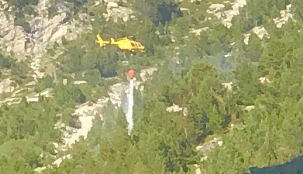 Un helicóptero arroja agua sobre una superficie arbolada para apagar un incendio en Panticosa.