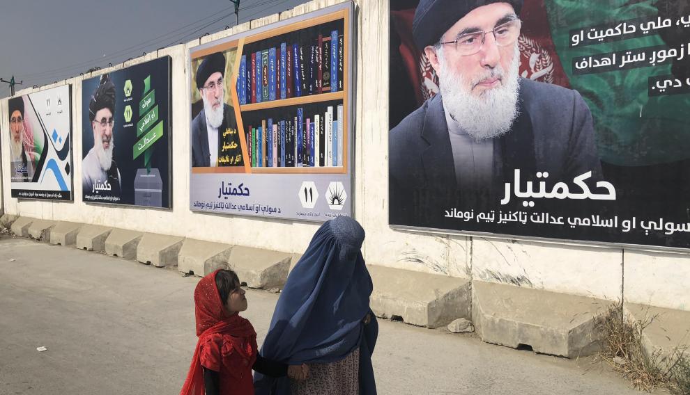 Una mujer con burka y una niña pasan por un muro con publicidad electoral del señor de la guerra Gulbudin Hekmatyar