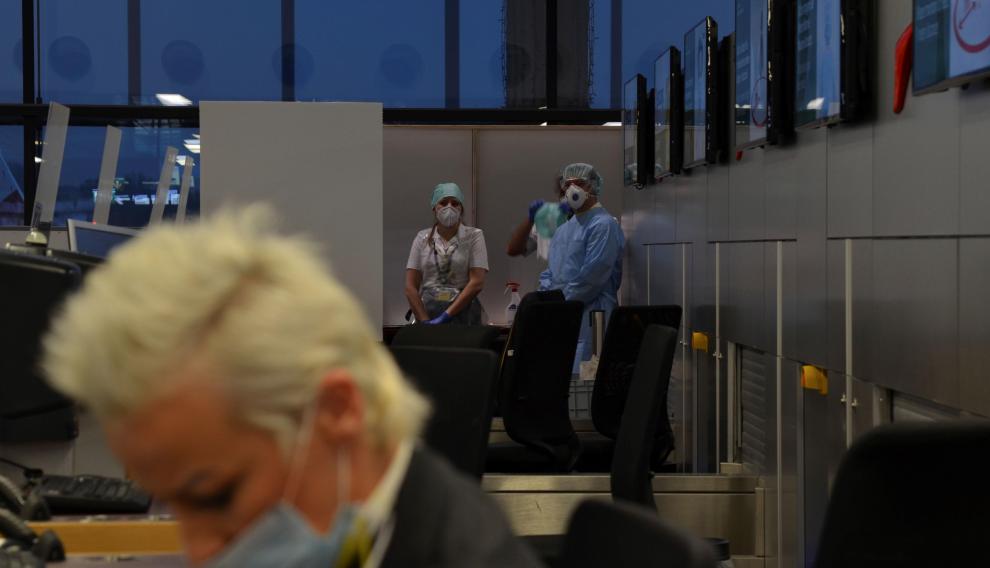 Una empleada del aeropuerto de Viena factura maletas mientras dos especialistas esperan para realizar test rápidos de antígenos.