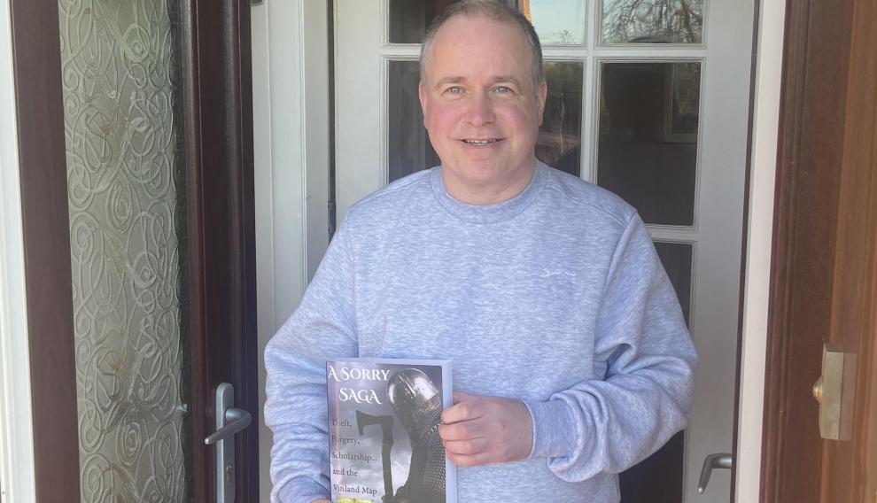 John Paul Floyd, a la puerta de su casa y con un ejemplar de su libro en las manos.