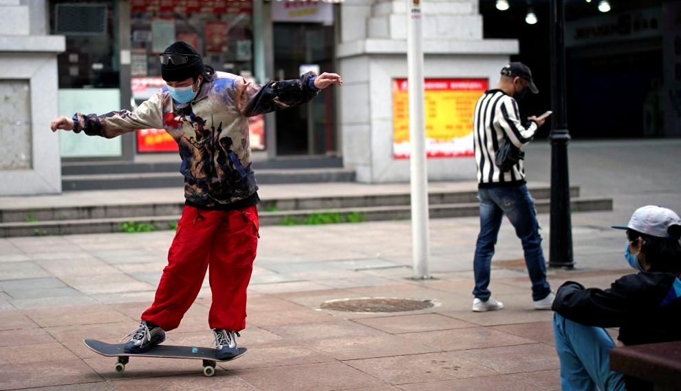 Un joven con mascarilla juega con un monopatín en Wuhan.