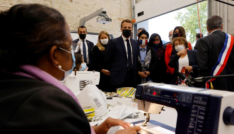 French President Emmanuel Macron talks with people sewing face masks during his visit to the Ateliers du Moulin, in Les Mureaux, near Paris