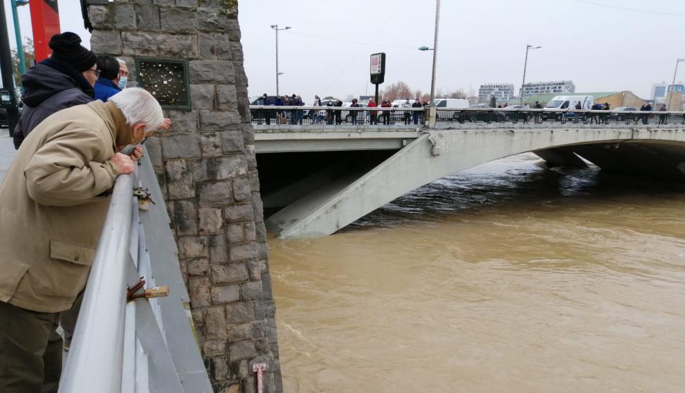 Un vecino de Zaragoza se asoma para ver la altura del caudal que alcanza el Ebro a su paso por el puente de Santiago.