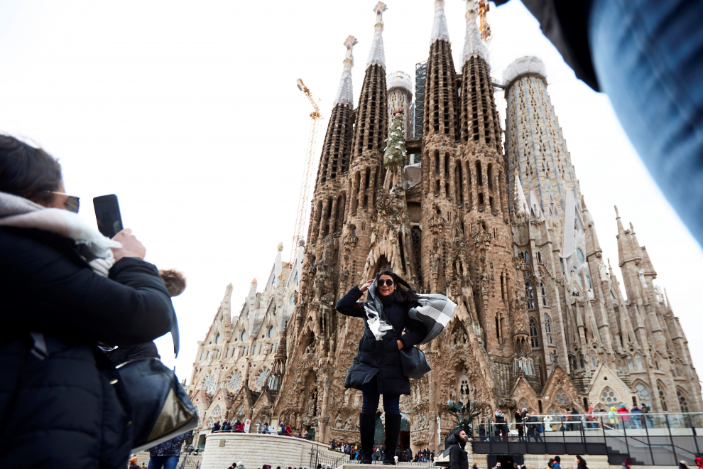 Unos turistas se fotografían bajo la Sagrada Familia de Barcelona en medio del temporal de viento
