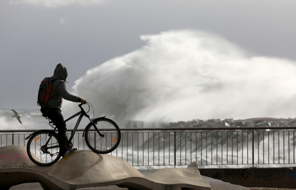 Un ciclista observa las enormes olas en la playa de la Barceloneta.