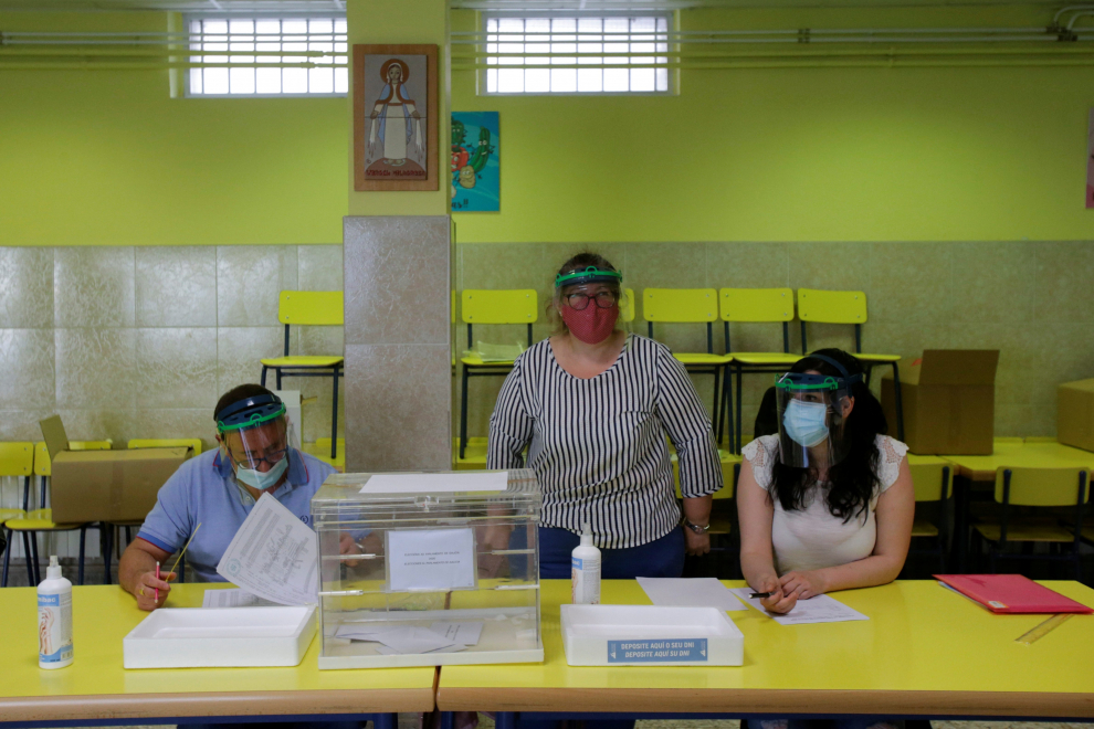 Officials, wearing protective face masks, wait for voters at a polling station during Galicia's regional elections in Ribadeo