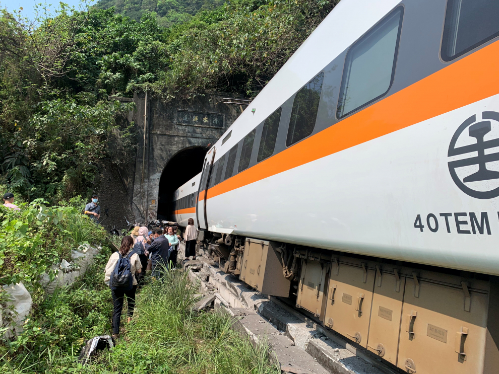 People walk next to a train which derailed in a tunnel north of Hualien