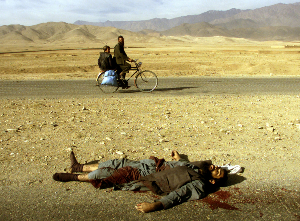 Año 2001. Un hombre en bicicleta con un niño pasa junto a un talibán muerto en combate