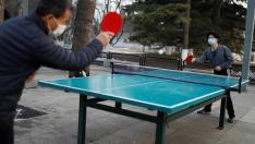 Dos personas con mascarilla juegan al tenis de mesa en un parque de Pekín