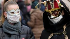 Dos personas pasean por Venecia con máscaras de carnaval y mascarillas protectoras.