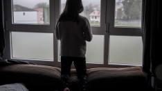 Una niña asomada a la ventana de su casa.