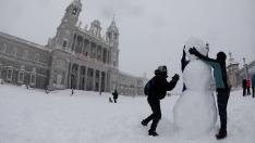 Dos personas hacen un muñeco de nieve en las inmediaciones de la Catedral de la Almudena, en Madrid.