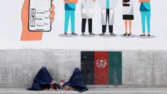 FILE PHOTO: Afghan women clad in burqa Beg under graffiti on a wall, in Kabul
