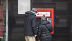 Una pareja de jubilados operan en el cajero automático de una entidad bancaria en Zaragoza.