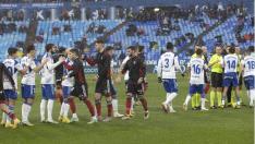 Los futbolistas de ambos equipos se saludan antes del partido, bajo un intenso aguacero sobre Zaragoza.