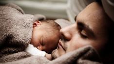 Un padre duerme junto a su bebé.