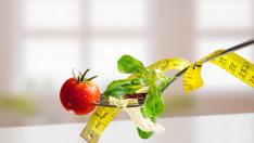 Salad with lettuce and tomato on a metal fork with tape on white table and windows background. Concept of healthy diet and nutrition. Front view, Horizontal composition.
