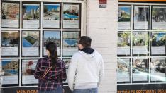 Una pareja mira anuncios de pisos en una inmobiliaria.