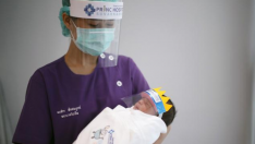 Un sanitario junto a un bebé con mascara por el covid-19.
