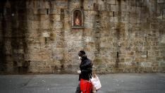 Una persona protegida contra el virus pasa por delante de la imagen de San Fermín en el primer tramo del encierro