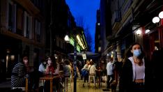 FILE PHOTO: People wearing protective masks walk past bar customers after bars reopened in Spain's Basque Country, amid the coronavirus disease (COVID-19) outbreak, in Bilbao