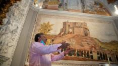 El alcalde de Bijuesca explica cómo es la romería de la Saca de la Virgen ante una pìntura de la ermita que la reproduce