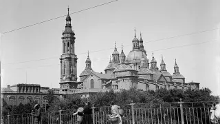 Vista del templo del Pilar de Zaragoza (fue Basílica en 1948), con solo dos torres, desde el puente de Piedra en 1929. En la fotografía, se ve como las mujeres cruzaban el puente, cargadas con sus cestas, para ir a atender sus faenas. La barandilla metálica colocada en 1908 pervivió en el puente hasta 1991