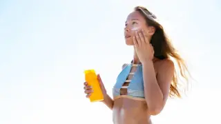 Chica poniéndose crema en la cara en la playa.