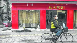 Un hombre pasa por la calle con una bicicleta en Wuhan (China), junto a un anciano fallecido por el Coronavirus.