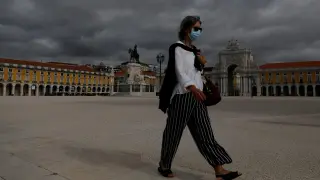 Una mujer protegida con una máscara camina por una vacía plaza del Comercio, en Lisboa.