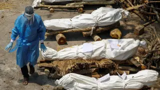 Un sanitario indio pasa entre cadáveres de fallecidos por covid.