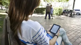 Una joven lee en un libro electrónico en un banco, en una imagen de archivo.