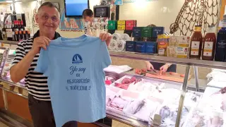 Fernando Mompradré, en la pescadería que lleva su nombre en Huesca, posa con la camiseta que repartirá entre sus clientes para reivindicar la supervivencia de este tipo de comercios especializados.