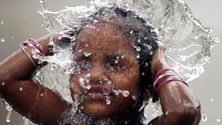 Una niña se baña bajo un chorro de agua en Ahmedabad, en la India.