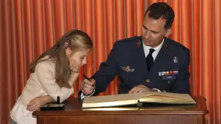 Leonor de Borbón mira como su padre don Felipe firma un libro durante la entrega de despachos de Teniente a la XLI promoción de la Academia General del Aire en Murcia, el 2 de mayo de 2014. Gran parte del aprendizaje de la Princesa de Asturias se ha producido con el ejemplo de su padre.
