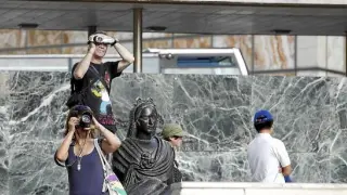 Dos turistas, cámara en mano, inmortalizan la plaza del Pilar de Zaragoza.