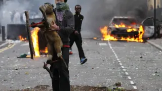 Un joven sujeta un juguete frente a un coche ardiendo