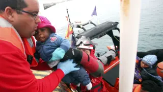 Un responsable de Cruz Roja sube a un bebe de a bordo de una patera