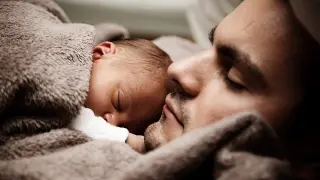 Un padre duerme junto a su bebé.