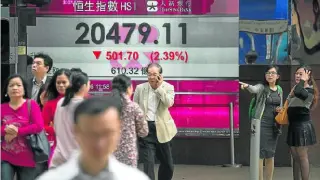 Varias personas caminan junto a una pantalla que muestra el índice Hang Seng, ayer en Hong Kong (China).