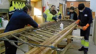 Varios alumnos del taller de carpintería decapando una barandilla.