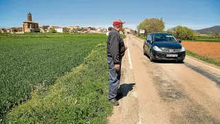 Un vecino observa el paso de un coche por la carretera autonómica, con Mainar al fondo.