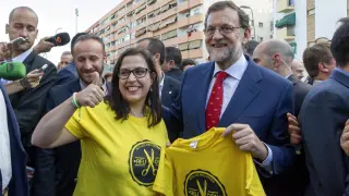 El presidente del Gobierno en funciones y candidato del PP a la reelección, Mariano Rajoy (d), con una simpatizante que lleva una camiseta de 'No a los recortes Religión'