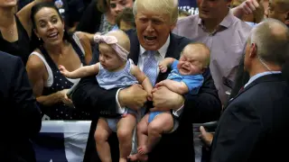 Trump sosteniendo a dos bebés en un acto de campaña.