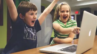 Dos niños jugando a un vídeojuego en un ordenador portátil.